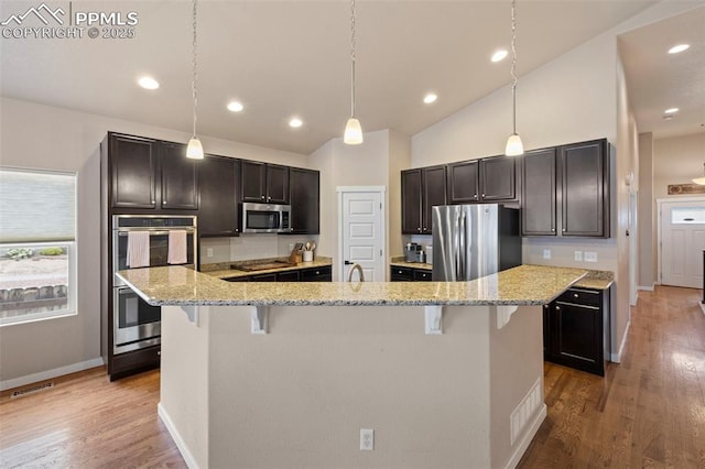 6374 Tramore Way, Colorado Springs, CO 80923 - kitchen featuring appliances with stainless steel finishes, a breakfast bar, light stone counters, wood finished floors, and vaulted ceiling
