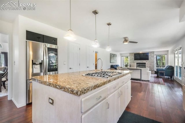1240 Lone Scout Lookout, Monument, CO 80132 - kitchen with stainless steel appliances, dark wood-style flooring, a ceiling fan, a fireplace, and light stone countertops