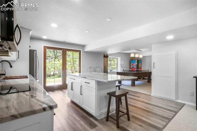 1240 Lone Scout Lookout, Monument, CO 80132 - kitchen featuring appliances with stainless steel finishes, white cabinets, a kitchen bar, light stone countertops, and light wood-type flooring