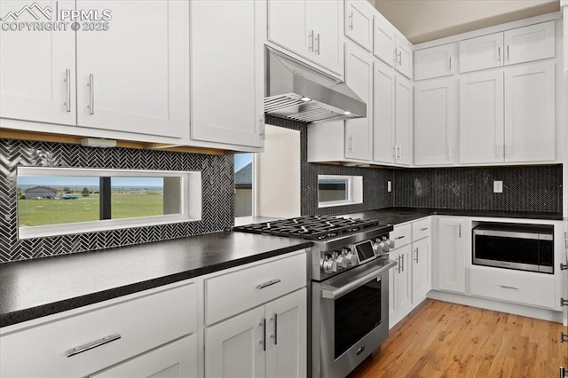 8545 Bailiff Dr, Peyton, CO 80831 - kitchen with stainless steel appliances, under cabinet range hood, dark countertops, tasteful backsplash, and white cabinetry