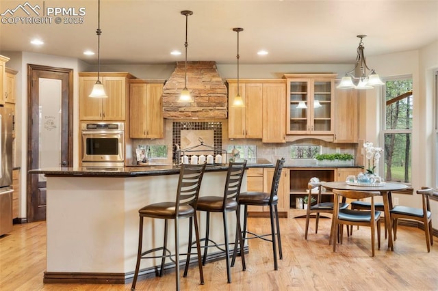 8395 Bar X Ter, Colorado Springs, CO 80908 - kitchen featuring light brown cabinets, decorative backsplash, a kitchen breakfast bar, glass insert cabinets, and light wood finished floors