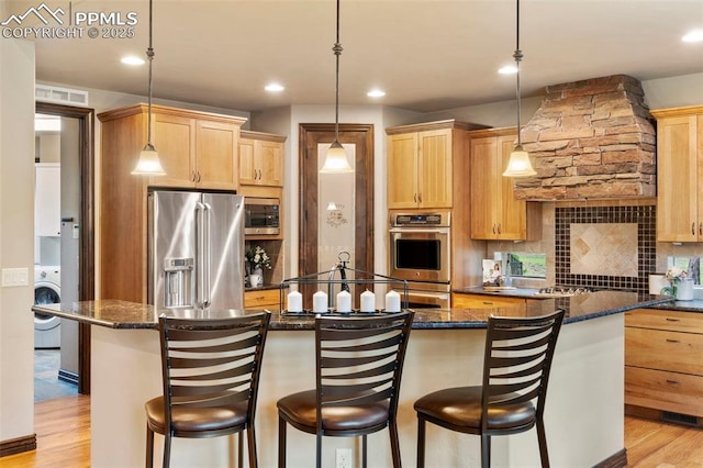 8395 Bar X Ter, Colorado Springs, CO 80908 - kitchen featuring stainless steel appliances, washer / dryer, a kitchen island with sink, light wood-style floors, and recessed lighting
