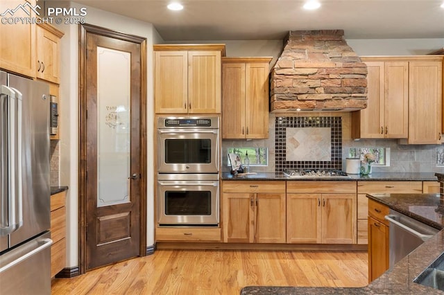 8395 Bar X Ter, Colorado Springs, CO 80908 - kitchen featuring appliances with stainless steel finishes, custom range hood, dark stone countertops, light wood finished floors, and decorative backsplash
