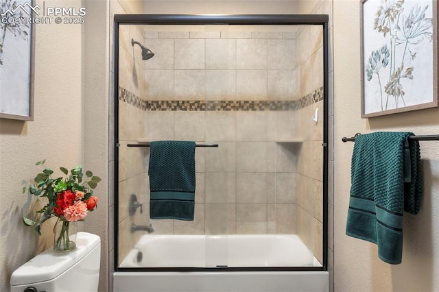 8395 Bar X Ter, Colorado Springs, CO 80908 - bathroom featuring shower / bath combination with glass door, a textured wall, and toilet