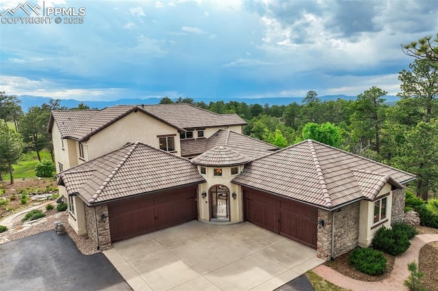 5085 Saxton Hollow Rd, Colorado Springs, CO 80908 - view of front facade with an attached garage, concrete driveway, stone siding, a tiled roof, and stucco siding