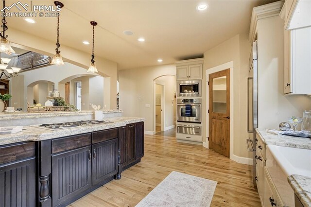 5085 Saxton Hollow Rd, Colorado Springs, CO 80908 - kitchen with stainless steel appliances, a warming drawer, arched walkways, light wood finished floors, and hanging light fixtures