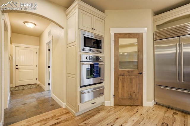 5085 Saxton Hollow Rd, Colorado Springs, CO 80908 - kitchen featuring built in appliances, a warming drawer, arched walkways, light wood-style floors, and cream cabinets
