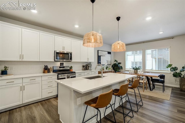 6950 Hidden Cove Ct, Castle Pines, CO 80108 - kitchen with stainless steel appliances, a sink, white cabinets, a kitchen island with sink, and wood finished floors