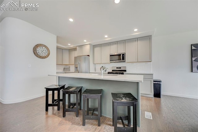 9276 Glitter Way, Colorado Springs, CO 80924 - kitchen with appliances with stainless steel finishes, gray cabinetry, light wood-style flooring, a kitchen bar, and recessed lighting