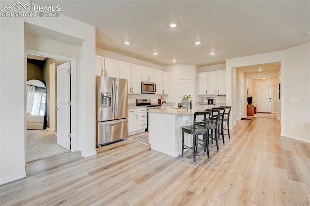 10806 Rolling Peaks Dr, Peyton, CO 80831 - kitchen with stainless steel appliances, light wood-style flooring, white cabinets, a kitchen bar, and recessed lighting