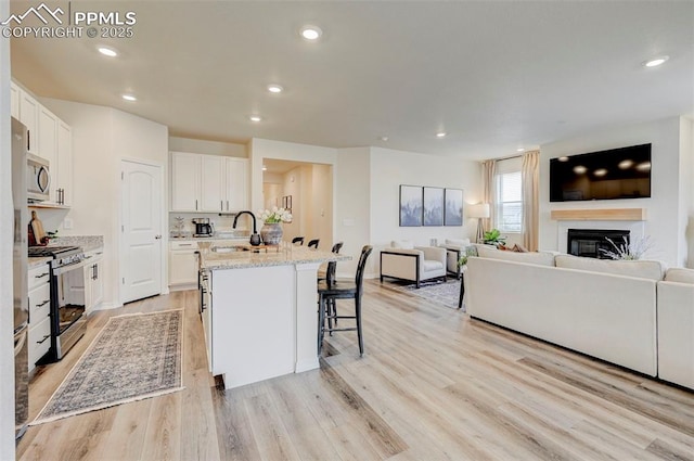 10806 Rolling Peaks Dr, Peyton, CO 80831 - kitchen with appliances with stainless steel finishes, open floor plan, an island with sink, a glass covered fireplace, and recessed lighting