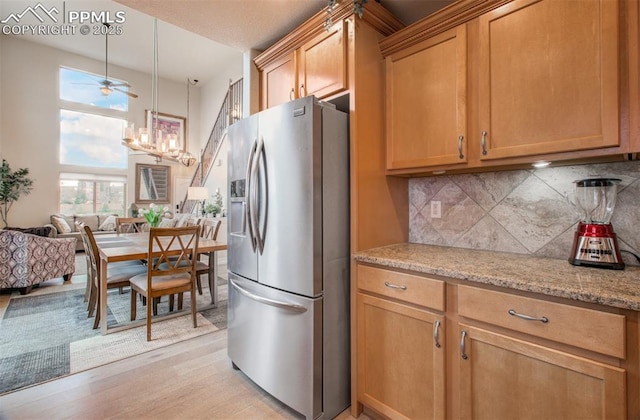 2582 Indian Hills Grv, Colorado Springs, CO 80907 - kitchen with stainless steel fridge, backsplash, light stone countertops, a chandelier, and light wood finished floors