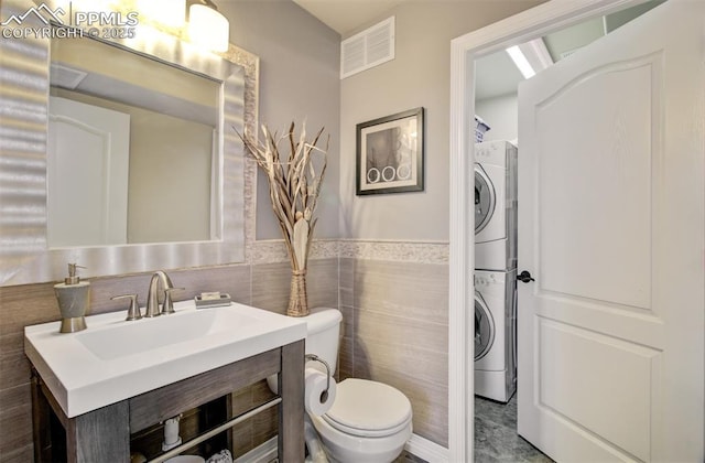 2582 Indian Hills Grv, Colorado Springs, CO 80907 - bathroom featuring stacked washer / drying machine, toilet, tile walls, vanity, and a wainscoted wall