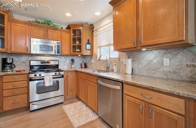 2582 Indian Hills Grv, Colorado Springs, CO 80907 - kitchen with stainless steel appliances, a sink, light stone counters, brown cabinetry, and light wood-style floors