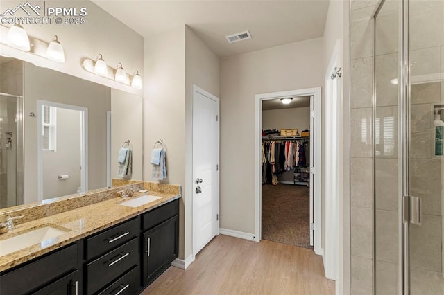 13138 Stoney Meadows Way, Peyton, CO 80831 - bathroom with a stall shower, double vanity, wood finished floors, a walk in closet, and baseboards