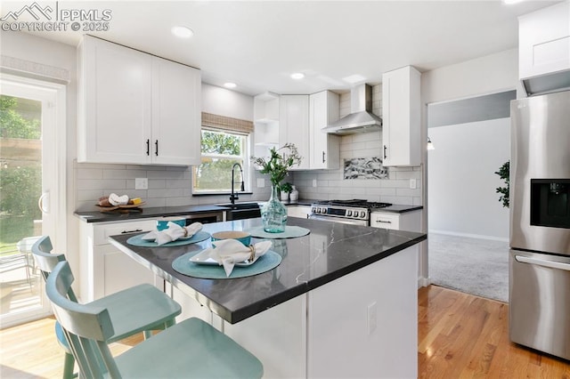 531 Saber Creek Dr, Monument, CO 80132 - kitchen featuring appliances with stainless steel finishes, wall chimney range hood, dark countertops, white cabinetry, and light wood-style flooring
