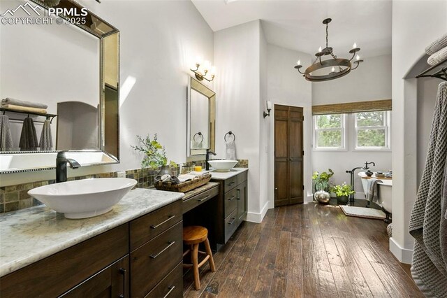 3320 Camels Ridge Ln, Colorado Springs, CO 80904 - bathroom featuring two vanities, wood-type flooring, a soaking tub, decorative backsplash, and a high ceiling