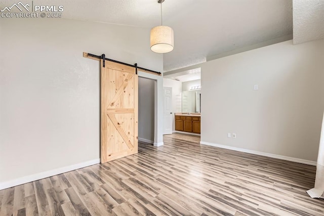 9412 Dew Drop Ct, Colorado Springs, CO 80925 - unfurnished bedroom featuring light wood-type flooring, baseboards, a barn door, connected bathroom, and a textured ceiling