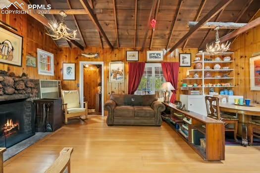 6015 Sioux Trl, Cascade, CO 80809 - living room with a chandelier, wood finished floors, wood walls, a warm lit fireplace, and wood ceiling
