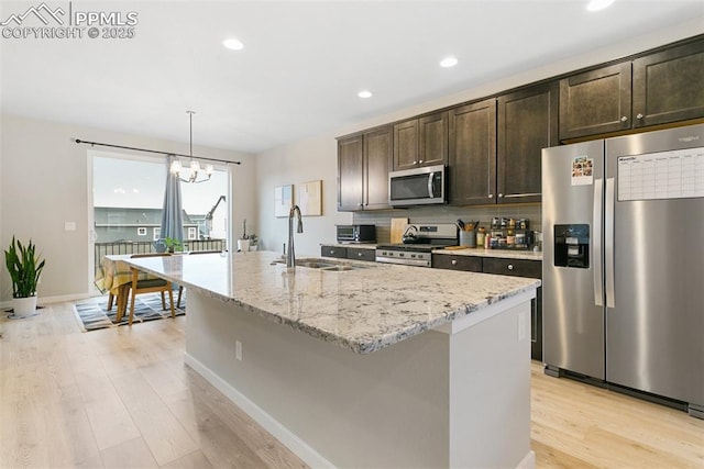 6697 Cool Breeze Dr, Colorado Springs, CO 80923 - kitchen with stainless steel appliances, light wood-style flooring, dark brown cabinetry, a center island with sink, and light stone countertops