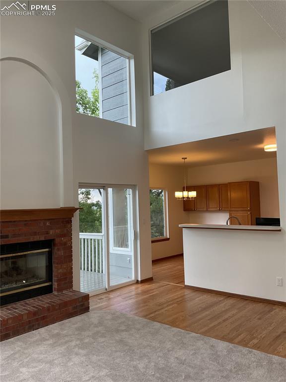 1185 Marlstone Pl, Colorado Springs, CO 80904 - unfurnished living room with plenty of natural light, carpet flooring, a chandelier, a high ceiling, and a brick fireplace
