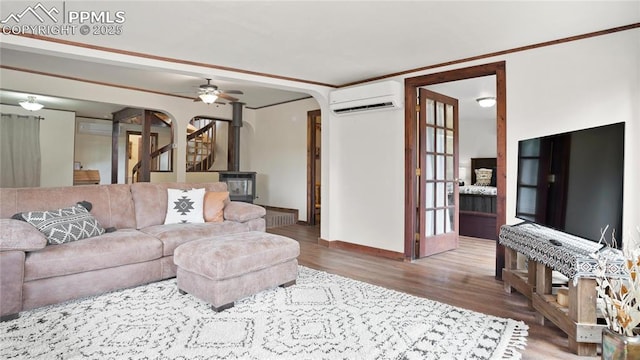 145 Valley Ln, Woodland Park, CO 80863 - living room featuring a wall mounted air conditioner, arched walkways, wood finished floors, a wood stove, and baseboards