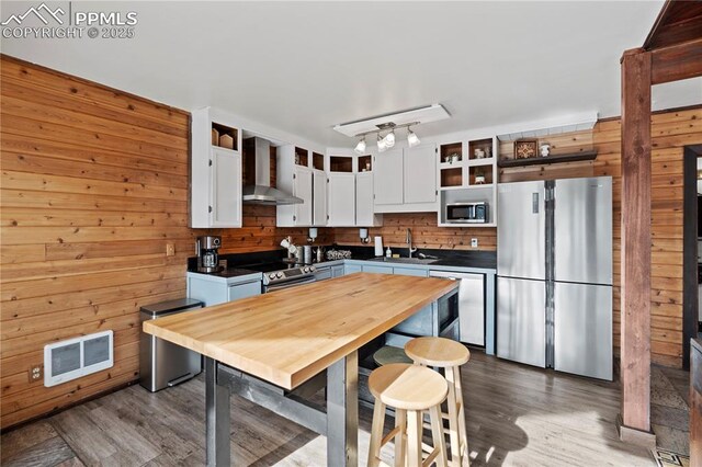 145 Valley Ln, Woodland Park, CO 80863 - kitchen with stainless steel appliances, wall chimney exhaust hood, dark wood-style flooring, wood walls, and white cabinets