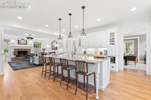 3 Mesa Ln, Colorado Springs, CO 80906 - kitchen with light wood-style flooring, a breakfast bar, white cabinetry, glass insert cabinets, and a center island with sink