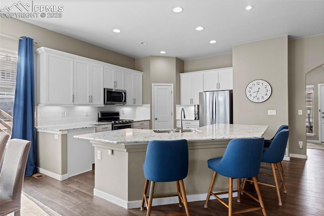 1734 Summerglow Ln, Monument, CO 80132 - kitchen with stainless steel appliances, a sink, dark wood finished floors, a kitchen island with sink, and white cabinetry