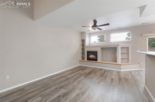 3867 Josephine Hts, Colorado Springs, CO 80906 - unfurnished living room with wood finished floors, a glass covered fireplace, a ceiling fan, and built in shelves