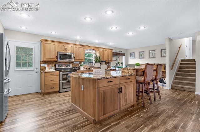 3512 Chico Cir, Colorado Springs, CO 80918 - kitchen with stainless steel appliances, wood finished floors, a center island, light stone counters, and a textured ceiling