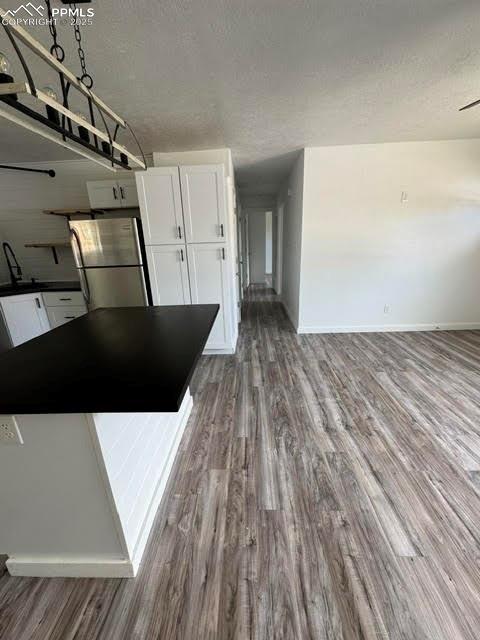 4425 Barkman Cir, Colorado Springs, CO 80916 - kitchen featuring freestanding refrigerator, white cabinets, wood finished floors, a textured ceiling, and dark countertops