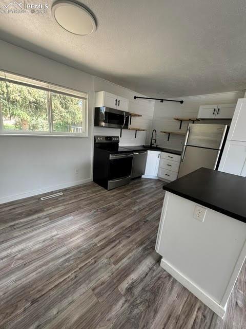 4425 Barkman Cir, Colorado Springs, CO 80916 - kitchen with appliances with stainless steel finishes, dark countertops, white cabinets, dark wood-style flooring, and a textured ceiling
