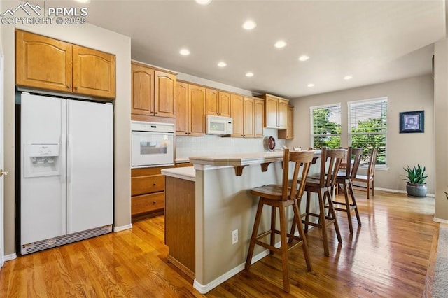 10290 Peach Blossom Trl, Colorado Springs, CO 80920 - kitchen with white appliances, light wood-style flooring, recessed lighting, a center island, and a breakfast bar