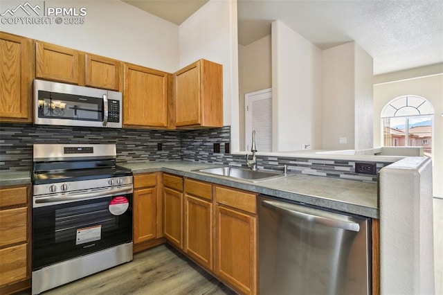 4710 Sand Mountain Pt, Colorado Springs, CO 80923 - kitchen with appliances with stainless steel finishes, backsplash, light wood finished floors, brown cabinetry, and a peninsula