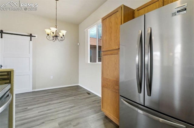 4710 Sand Mountain Pt, Colorado Springs, CO 80923 - kitchen featuring appliances with stainless steel finishes, a barn door, brown cabinetry, light wood-type flooring, and a chandelier