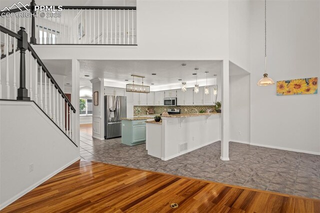 206 Luxury Ln, Colorado Springs, CO 80921 - kitchen with appliances with stainless steel finishes, dark wood-style floors, a towering ceiling, tasteful backsplash, and a breakfast bar area