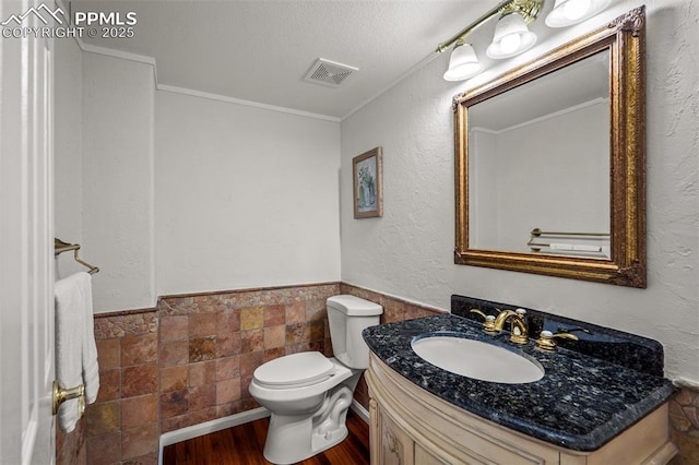 206 Luxury Ln, Colorado Springs, CO 80921 - half bathroom featuring wood finished floors, vanity, a wainscoted wall, tile walls, and a textured ceiling