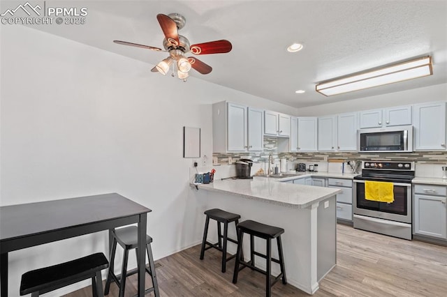 1749 Victorian Pt, Colorado Springs, CO 80905 - kitchen with appliances with stainless steel finishes, decorative backsplash, a breakfast bar, a peninsula, and light countertops