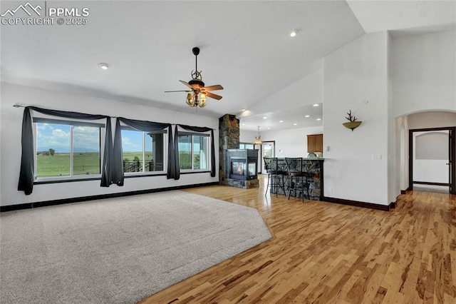 11354 Mckissick Rd, Peyton, CO 80831 - unfurnished living room with ceiling fan, arched walkways, light wood-type flooring, a stone fireplace, and high vaulted ceiling