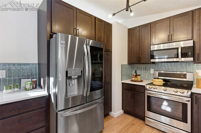 629 E Monument St, Colorado Springs, CO 80903 - kitchen with appliances with stainless steel finishes, dark brown cabinets, light wood-style flooring, light countertops, and tasteful backsplash