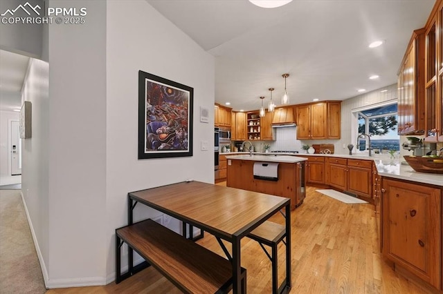 78 Raven Hills Ct, Colorado Springs, CO 80919 - kitchen with light countertops, a center island with sink, stainless steel microwave, brown cabinetry, and black stovetop