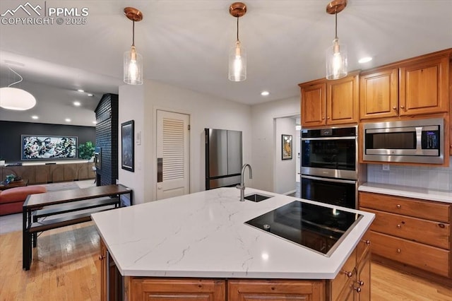 78 Raven Hills Ct, Colorado Springs, CO 80919 - kitchen featuring stainless steel appliances, light wood finished floors, open floor plan, brown cabinetry, and an island with sink