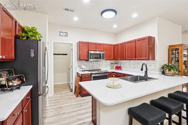 7845 Morning Dew Rd, Colorado Springs, CO 80908 - kitchen featuring appliances with stainless steel finishes, reddish brown cabinets, a peninsula, light wood-style floors, and backsplash