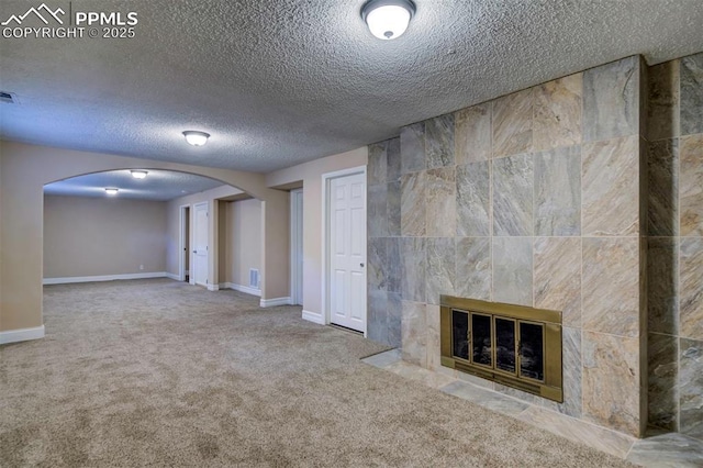 2928 Nevermind Ln, Colorado Springs, CO 80917 - unfurnished living room featuring arched walkways, a textured ceiling, carpet floors, and a tiled fireplace
