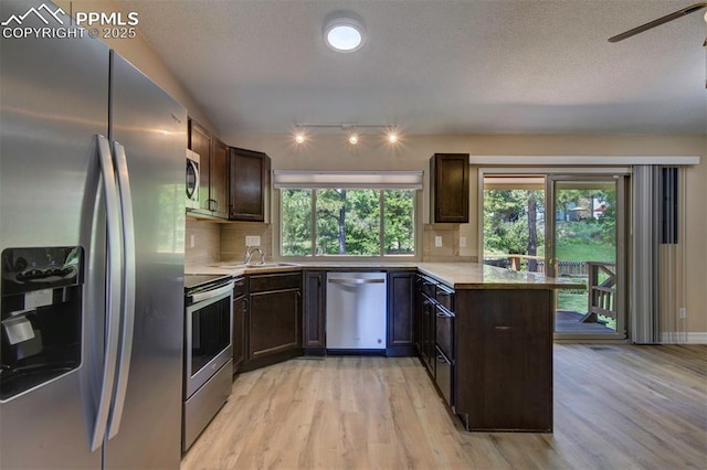2928 Nevermind Ln, Colorado Springs, CO 80917 - kitchen featuring stainless steel appliances, light wood-style floors, a peninsula, dark brown cabinets, and a textured ceiling