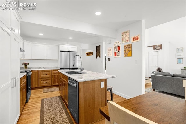 55 Woodbridge Dr, Colorado Springs, CO 80906 - kitchen featuring stainless steel appliances, light wood finished floors, white cabinetry, a kitchen bar, and a kitchen island with sink