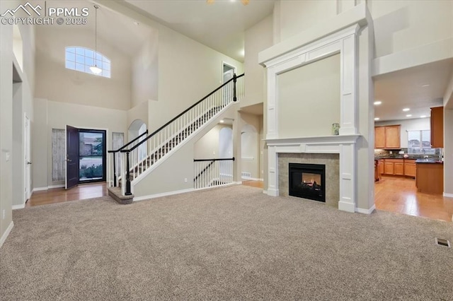 13080 Mt Harvard Dr, Peyton, CO 80831 - unfurnished living room featuring a towering ceiling, light carpet, a fireplace, and stairs