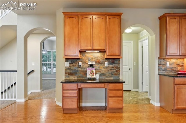 13080 Mt Harvard Dr, Peyton, CO 80831 - kitchen featuring light wood finished floors, tasteful backsplash, dark stone countertops, arched walkways, and brown cabinets