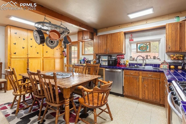 125 1st St, Saguache, CO 81149 - kitchen with stainless steel appliances, tile counters, light floors, beam ceiling, and brown cabinetry
